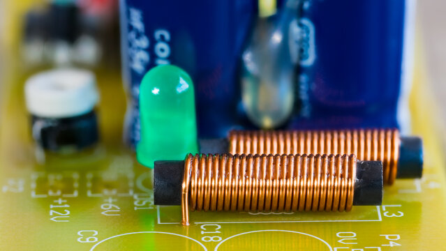 Electromagnetic coils, green LED light and electronic components on printed circuit board. Closeup of cylindric inductors with spiral copper wire on ferrite core or light-emitting diode on yellow PCB.