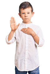 Cute blond kid wearing elegant shirt swearing with hand on chest and open palm, making a loyalty promise oath