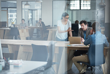 They make business happen. Through the glass shot of a group of colleagues working together in an office.
