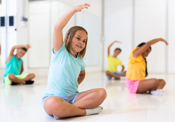 Little girl warming up with group of children in dance class, doing stretching exercises before...