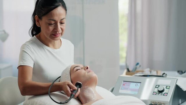Video of  cosmetologist makes the procedure an ultrasonic cleaning of the facial skin of a beautiful young woman on the spa center.