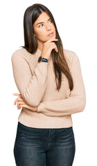 Young brunette woman wearing casual winter sweater with hand on chin thinking about question, pensive expression. smiling with thoughtful face. doubt concept.