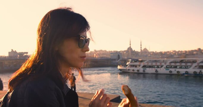 Woman eating turkish bagel with istanbul city view at sunrise light, static medium shot
