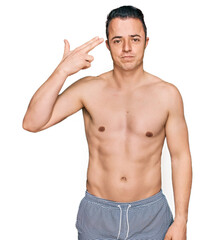 Fototapeta premium Handsome young man wearing swimwear shirtless shooting and killing oneself pointing hand and fingers to head like gun, suicide gesture.