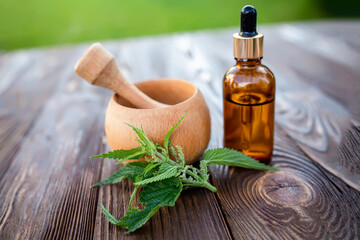 Elexir and nettle essential oil. Wooden mortar and cosmetic jar with dispenser on the table near a leaf of fresh nettle