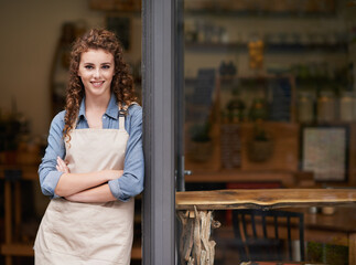 Shes proud of her little shop. A young woman standing in her store doorway.