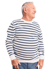 Obraz premium Senior handsome grey-haired man wearing casual striped sweater looking away to side with smile on face, natural expression. laughing confident.