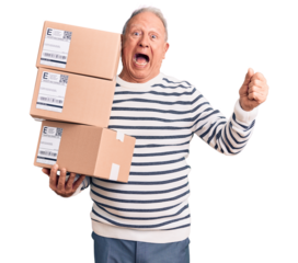Senior handsome grey-haired man holding delivery boxes screaming proud, celebrating victory and success very excited with raised arms