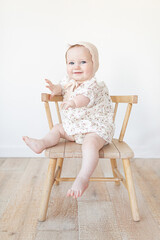 baby with a limb difference disability sitting in a wooden chair with a bonnet and floral dress