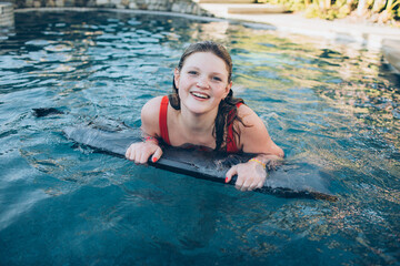 teenage girl with freckles and wet hair in red bathing suit in a pool during the summer