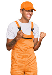 Young handsome african american man wearing handyman uniform excited for success with arms raised...