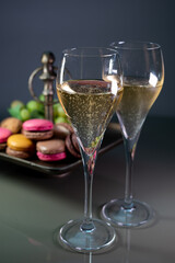 Glasses of sparkling white wine champagne or cava with bubbles and sweet dessert colorful macarons biscuits on background