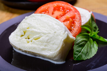 Sliced white ball of Italian soft cheese Mozzarella di Bufala Campana served with fresh green basil and red tomato