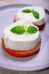 Sliced white ball of Italian soft cheese Mozzarella di Bufala Campana served with fresh green basil and red tomato