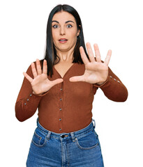 Young hispanic woman wearing casual clothes afraid and terrified with fear expression stop gesture with hands, shouting in shock. panic concept.