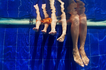 Happy people relaxing with fun. Funny underwater photo mother with kids legs in aqua park swimming pool. Family lifestyle and summer children water sports activity and lessons with parents on vacation