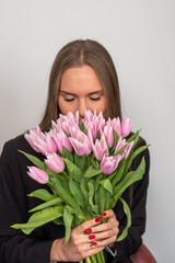 A young business woman in a black suit smells a bouquet of pink tulips on a white background. Anniversary of meeting, celebration of love. Advertising poster, space for your text