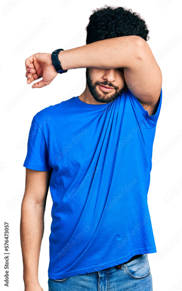 Sticker Young arab man with beard wearing casual blue t shirt covering eyes with arm, looking serious and sad. sightless, hiding and rejection concept