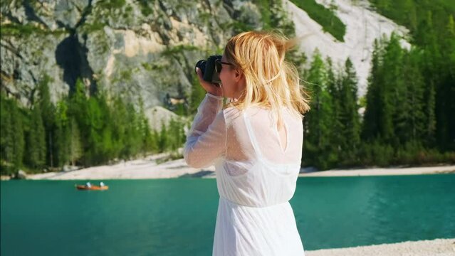 Woman in white dress takes photos of lake Braies and mountains with retro camera
