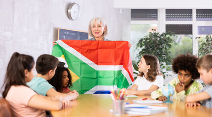 in geography lesson, pupils carefully listen to woman teacher who talks about South Africa