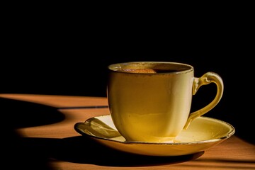Taza clásica de café expresso caliente, sobre mesa de madera, a la luz de una fría mañana.
