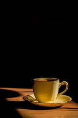 Taza clásica de café expresso caliente, sobre mesa de madera, a la luz de una fría mañana.
