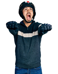 Young hispanic man with beard wearing motorcycle helmet doing driving gesture angry and mad screaming frustrated and furious, shouting with anger looking up.
