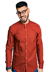 Young hispanic man with beard wearing business shirt and glasses winking looking at the camera with sexy expression, cheerful and happy face.