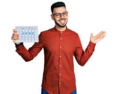 Young hispanic man with beard holding travel calendar celebrating achievement with happy smile and winner expression with raised hand