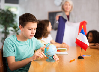 Fototapeta premium Mature female teacher holds the national flag of France and tells the pupils the history of the country