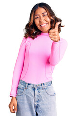 Young beautiful mixed race woman wearing pink shirt smiling happy and positive, thumb up doing excellent and approval sign
