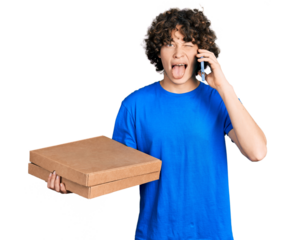 Caucasian teenager holding delivery package and talking by the smartphone sticking tongue out happy with funny expression.