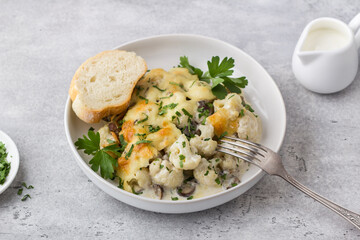 Baked cauliflower with mushrooms, cream and cheese sprinkled with parsley served with a slice of fresh bread and sour cream on a gray textured background