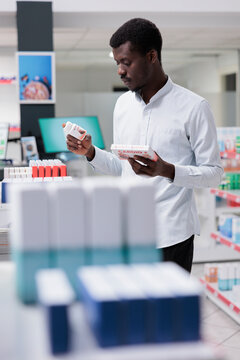 Young African American Taking Cardiovascular Supplements From Drugstore Shelf, Holding Two Heart Medication Packages, Checking Instruction. Customer Buying Medicaments, Choosing Prescription Treatment