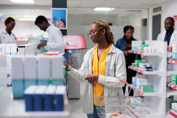 African american woman buying medications in drugstore, holding tablets package. Client choosing pills, customer standing in pharmacy aisle, pharmaceutical business, medicaments retail concept