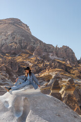 A sexy young traveler girl is sitting on a mountain against the backdrop of Turkish Cappadocia.