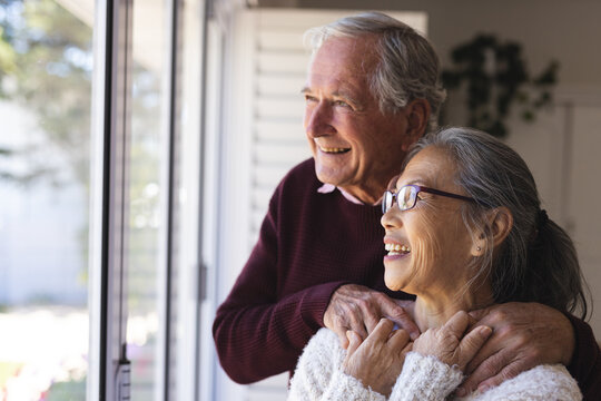 Happy senior diverse couple embracing and looking through window - Powered by Adobe