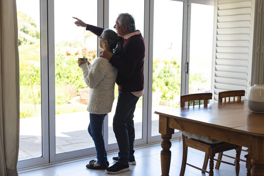 Happy senior diverse couple embracing and looking through window