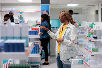African american woman checking medications in drugstore shelf, looking at tablet packages. Client...