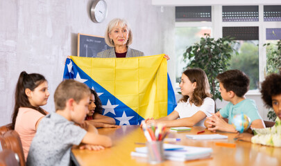 in geography lesson, students carefully listen to woman teacher who talks about Bosnia and...
