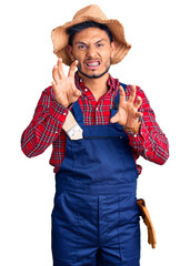 Handsome latin american young man weaing handyman uniform smiling funny doing claw gesture as cat, aggressive and sexy expression