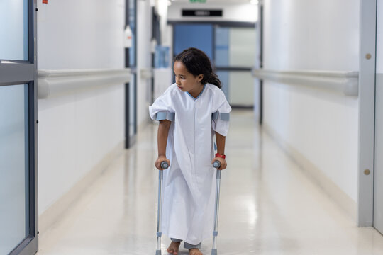 Biracial girl walking on crutsches in hospital corridor alone
