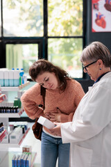 Obraz premium Drugstore employee helping sick customer with abdominal cramps offering stomachache painkillers while working in pharmacy. Client having gastritis looking for pills to cure food poisoning