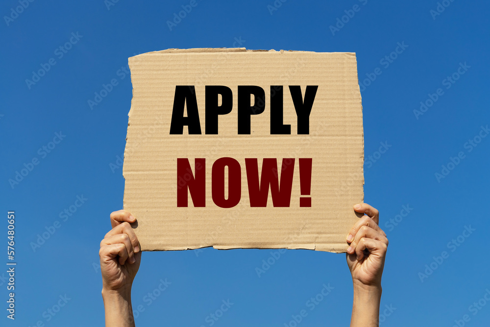 Poster apply now text on box paper held by 2 hands with isolated blue sky background. this message board ca