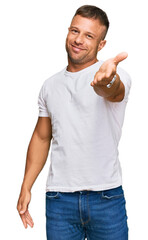 Handsome muscle man wearing casual white tshirt smiling cheerful offering palm hand giving...