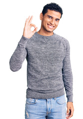 Hispanic handsome young man wearing casual sweater smiling positive doing ok sign with hand and fingers. successful expression.