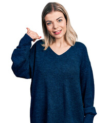 Young blonde woman wearing casual sweater smiling doing phone gesture with hand and fingers like talking on the telephone. communicating concepts.