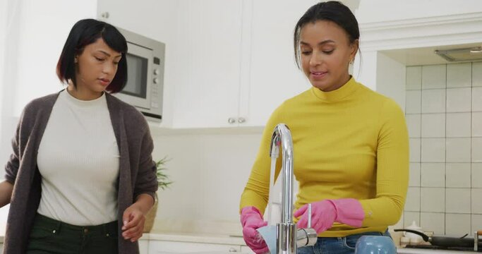Happy biracial sisters cleaning in kitchen, in slow motion