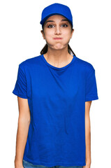 Young hispanic girl wearing delivery courier uniform puffing cheeks with funny face. mouth inflated with air, crazy expression.