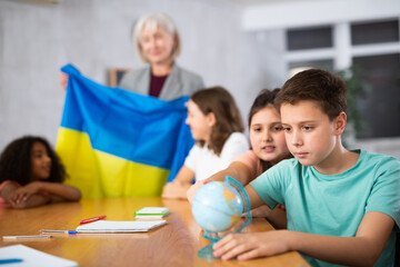 Portrait of an attentive schoolboy, studying the history of Ukraine in the lesson and looking for it on the globe